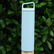 Load image into Gallery viewer, blue stainless steel water bottle with carry handle lid on fence post outdoors with foliage in the background
