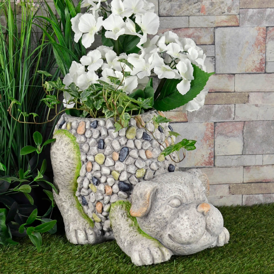 crouching dog garden planter in grey and brown mosaic pebble design filled with white flowers and ivy in a garden