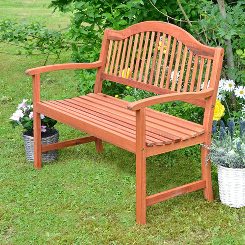 Wooden garden bench, traditional style with slatted back sitting on grass in a garden with flowers and plants