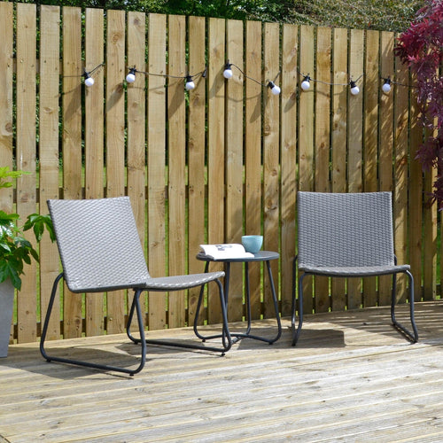 Grey metal garden bistro set with drak grey weave seats and a metal top side table on decking wit a coffee cup and book, on deecking with plants and sunshine