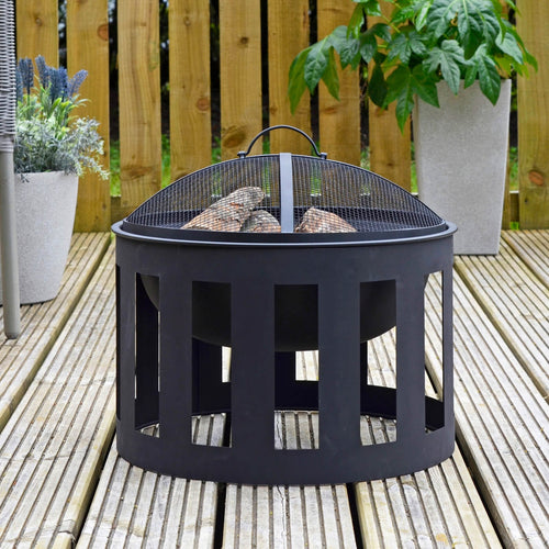 Black Vesta fire pit with steel mesh spark guard cover filled with logs ready for burning, sitting on decking area with plants and chair