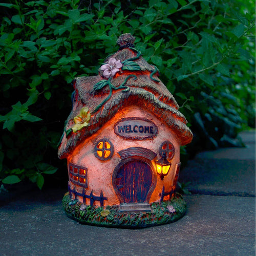 Welcome solar powered cottage garden decoration lit up, sitting on a paving stone next to green foliage