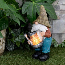 Load image into Gallery viewer, Solar power garden gnome decoration with light up watering can, lit up by LED lights, in a garden surrounded by plants and a stone wall
