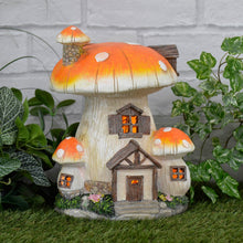 Load image into Gallery viewer, Solar mushroom house lit by orange lights sitting on grass with ivy, plants and a white brick wall
