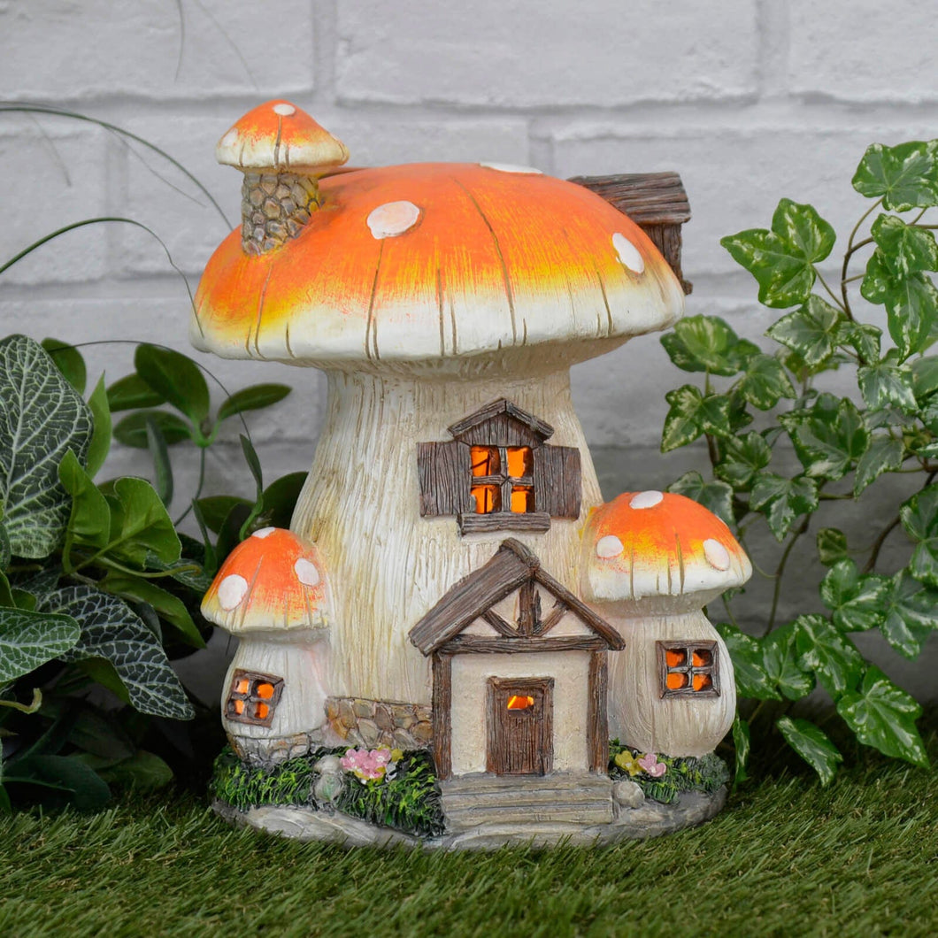 Solar mushroom house lit by orange lights sitting on grass with ivy, plants and a white brick wall