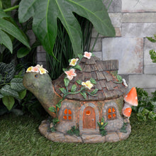 Load image into Gallery viewer, Solar power light up tortoise cottage with orange glow and flowers on grass in a garden with plants and stone wall
