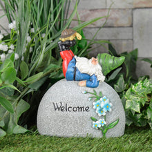 Load image into Gallery viewer, Garden gnome ornament, with grey stone pebble, Welcome text, blue flowers, figure with green hat and tortoise on his boots, in a garden with grass an dplants
