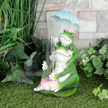 Load image into Gallery viewer, Novelty frog rain gauge with 2 frogs holding a glass measuring tube and a blue umbrella, sitting in a garden on the grass with ivy and a stone wall
