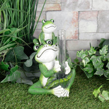 Load image into Gallery viewer, Novelty frog rain gauge with 2 frogs holding a glass measuring tube, sitting on the grass in a garden with plants and a stone wall
