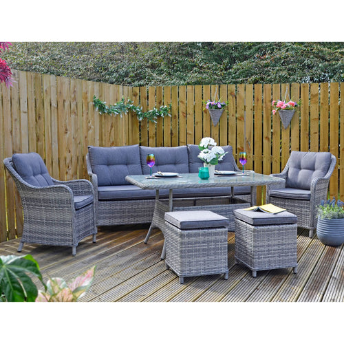 Grey rattan garden sofa set wth table and stools, on decking with flowers and plants