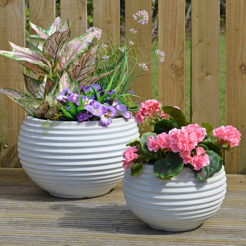 Light sand colour plastic planters with ridged design filled with flowers and plants in the sunshine on decking